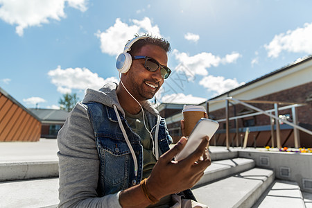 技术,休闲人的印度男子戴着耳机,智能手机顶部听音乐屋顶上智能手机耳机的男人图片