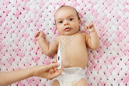 婴儿期,健康人的母亲的手与温度计测量温度的甜蜜小婴儿女儿尿布上躺针的粉红色毛毯毛绒纱母亲的手测量女婴的体温图片