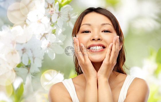 美丽,护肤人的快乐的微笑轻的亚洲妇女触摸她的脸自然春天樱花背景快乐微笑的亚洲轻女人抚摸她的脸图片