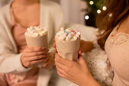 饮料,潮奇睡衣派的两个妇女女朋友着杯子与热巧克力棉花糖家里两个女人喝着棉花糖的热巧克力图片