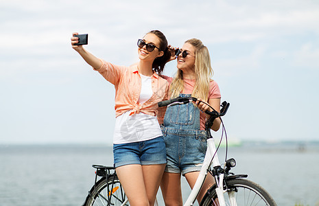 休闲,技术友谊的快乐微笑的十几岁女孩朋友骑自行车自拍智能手机海边夏天夏天自行车自拍的十几岁女孩图片