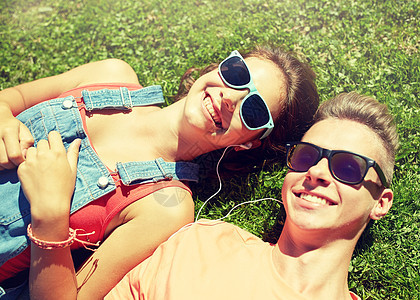 爱人的快乐的青少夫妇戴着太阳镜躺草地上,戴着耳机,夏天听音乐幸福的青少夫妇戴着耳机躺草地上图片