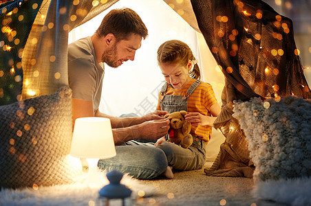 父亲与拿着泰迪熊玩具的小女儿在帐篷里玩玩具图片