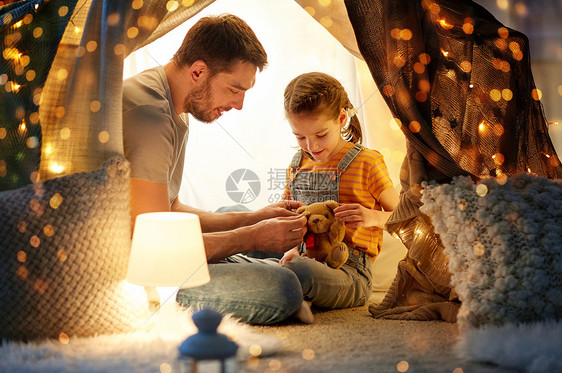 父亲与拿着泰迪熊玩具的小女儿在帐篷里玩玩具图片