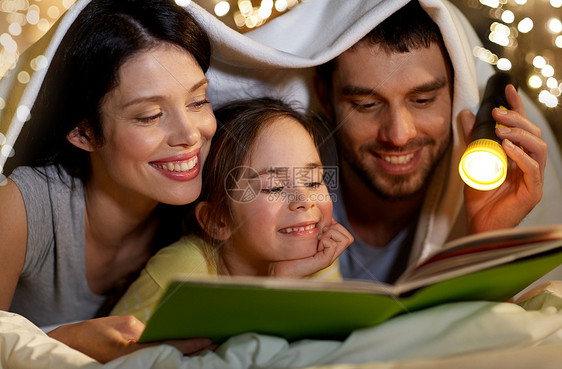 人们家庭的接近快乐的母亲,父亲小女儿阅读书籍与火炬灯床上晚上家毯子下快乐的家庭阅读书晚上床上家图片