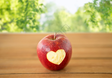 水果,食物健康成熟的红色苹果,雕刻的心形木制桌子上绿色的自然背景木桌上雕刻心形的红苹果图片