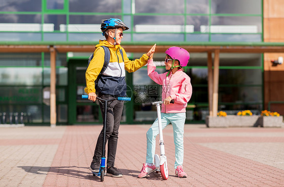 教育,童人的快乐的学校孩子戴着头盔,背包骑着滑板车,户外高五学校的孩子骑滑板车击掌图片