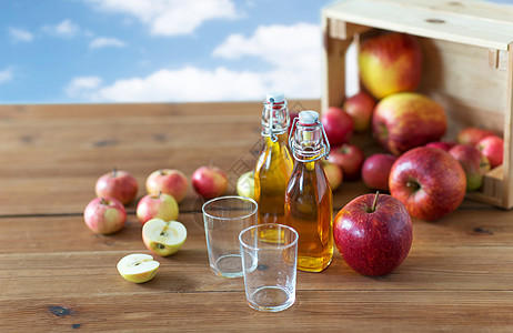 水果食物收获的两杯瓶子的苹果汁苹果酒木制桌子上蓝天云背景木制桌子上的眼镜苹果汁图片