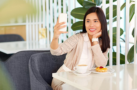 技术人的快乐的亚洲妇女与蛋糕咖啡自拍智能手机咖啡馆亚洲女人咖啡馆用智能手机自拍图片