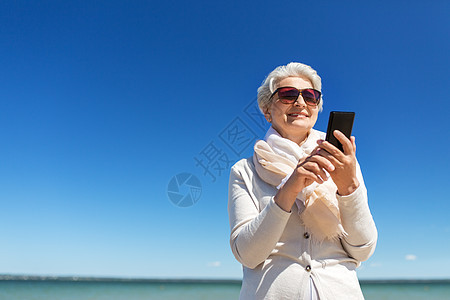 老人休闲快乐微笑的老年女子用智能手机爱沙尼亚海滩海滩上用智能手机的高级女人图片