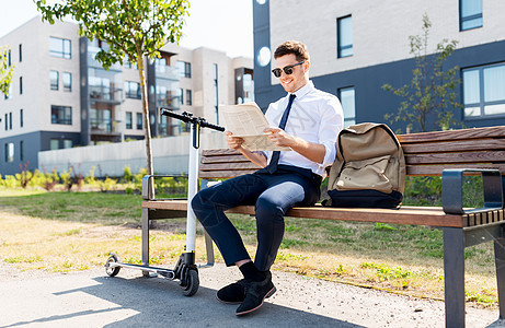 商业新闻企业人士轻的商人带着袋子,电动滑板车城市的街道长凳上阅读报纸商人与滑板车阅读报纸城市图片