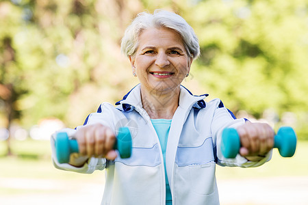 健身,运动健康的生活方式快乐的微笑老妇女与哑铃锻炼夏季公园戴哑铃的老妇女公园锻炼图片