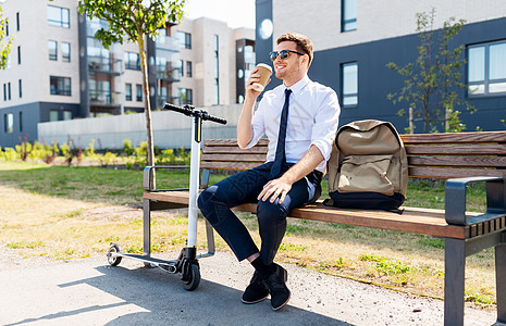 商业人轻的商人,带着袋子电动滑板车坐街上的长凳上,喝着外卖纸杯城市商人与滑板车城市喝咖啡图片