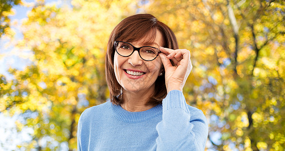视觉老人的秋天公园背景下戴眼镜的微笑的老妇女的肖像秋天公园里戴眼镜的老妇人的肖像背景图片