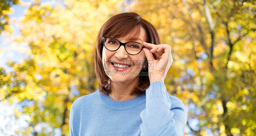 视觉老人的秋天公园背景下戴眼镜的微笑的老妇女的肖像秋天公园里戴眼镜的老妇人的肖像图片