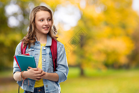 教育,学校人的快乐微笑的十几岁的学生女孩带着书包书秋天的公园背景带着书包的快乐微笑的十几岁的学生女孩图片
