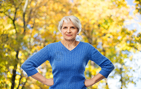 权力老人的老妇女的肖像,蓝色毛衣,双手臀部秋季公园背景秋季公园,位手放臀部的老年女子图片