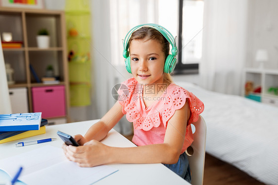 儿童,休闲技术快乐的学生女孩耳机与智能手机听音乐家里的办公桌戴耳机的女孩手机上听音乐图片