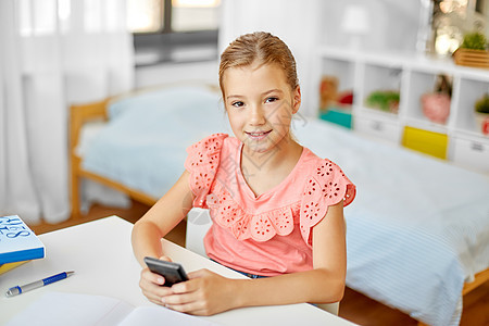 儿童,教育技术快乐的学生女孩家里用智能手机快乐的学生女孩家用智能手机图片