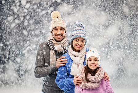 家庭,诞节冬天的衣服快乐的母亲,父亲小女儿戴着针帽围巾雪的背景下快乐的家庭穿着冬天的衣服雪的背景上背景图片