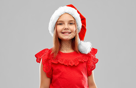 诞节,童假日的微笑的女孩摆斯纳塔帮手帽子灰色背景戴着斯纳塔帮手帽子的微笑女孩图片