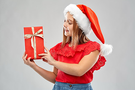 诞节,童假日微笑的女孩摆斯纳塔帮手帽子与礼品盒灰色背景带着诞礼物戴着Snata帽子的微笑女孩图片