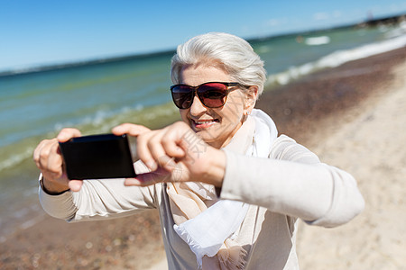 海滩照片老人休闲快乐微笑的老年女子爱沙尼亚海滩上用智能手机自拍高级女人海滩上用智能手机自拍背景