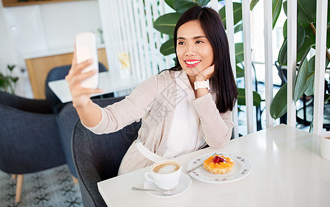 技术人的快乐的亚洲妇女与蛋糕咖啡自拍智能手机咖啡馆亚洲女人咖啡馆用智能手机自拍图片