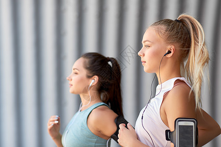 健身运动健康的生活方式轻女女朋友戴着带智能手机的,户外跑步带着耳机智能手机的轻女跑步图片