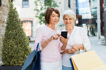 销售,消费主义人的两个老年女子朋友与购物袋智能手机塔林市街城里购物袋手机的老妇人图片