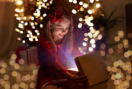 诞节,假期童的快乐的小女孩打开礼品盒与魔法灯黑暗中家里微笑的女孩晚上打开诞礼物图片