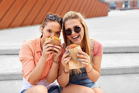 休闲,快餐友谊的快乐微笑的十几岁女孩最好的朋友戴着太阳镜城市街道上吃汉堡夏天十几岁的女孩朋友户外吃汉堡图片
