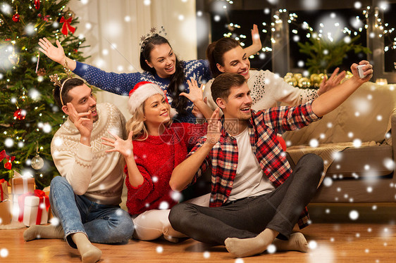 庆祝假期快乐的朋友戴着眼镜家里庆祝诞节,雪地上用智能手机自拍朋友们庆祝诞节自拍图片