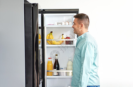 饮食饮食微笑的中男子厨房的冰箱里寻找食物厨房冰箱里找食物的人图片