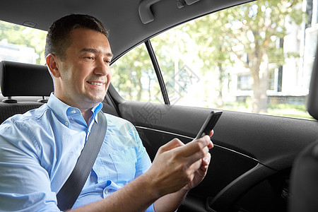 老年人手机运输商业通信微笑的男乘客商人用智能手机出租车后座乘客商人汽车中用智能手机背景