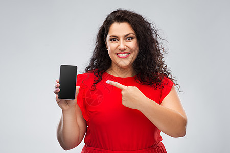 人物肖像快乐的女人穿着红色连衣裙,智能手机与空白屏幕灰色背景穿着红色连衣裙的快乐女人展示智能手机图片