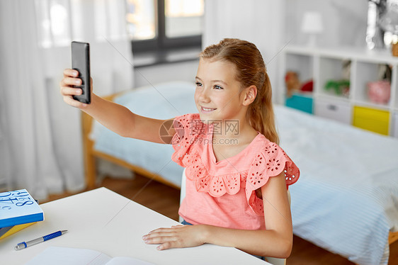 人,孩子技术女孩与智能手机自拍家快乐的女孩带着智能手机家里自拍图片
