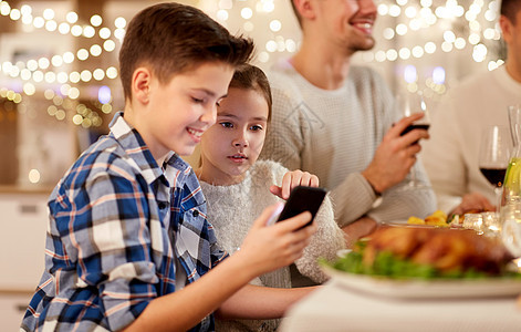 技术,假期人的快乐的男孩妹妹用智能手机家里举行家庭晚宴带妹妹的男孩家庭晚餐时用智能手机图片