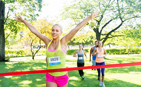 健身,运动成功的快乐的女人赢得比赛,并率先完成红色丝带超过运动员跑马拉松与章号码公园快乐的轻女跑步者完成获图片