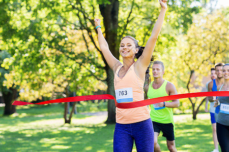 健身,运动成功的快乐的女人赢得比赛,并率先完成红色丝带超过运动员跑马拉松与章号码公园快乐的轻女跑步者完成获图片