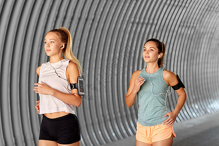 健身运动健康的生活方式轻女女朋友戴着带智能手机,户外跑步带着耳机智能手机的轻女跑步图片