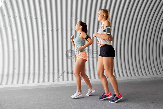 健身运动健康的生活方式轻女女朋友戴着带智能手机,户外跑步带着耳机智能手机的轻女跑步图片