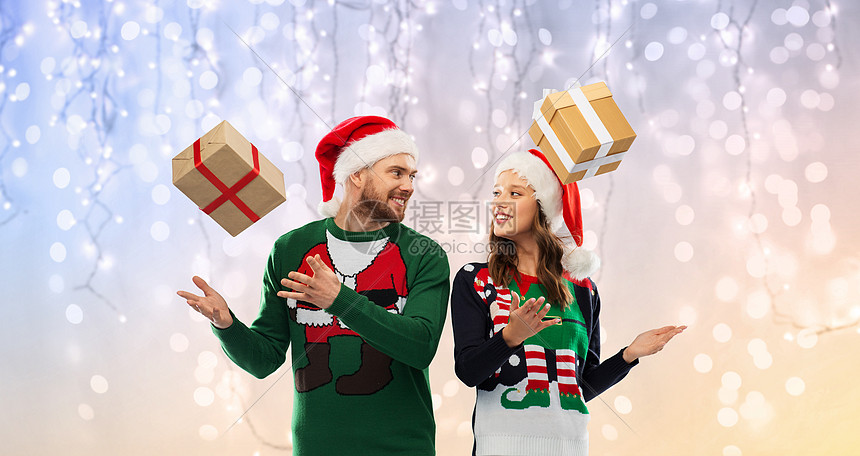 人们节日的幸福的夫妇戴着诞帽,毛衣派上节日的灯光背景诞毛衣里的幸福夫妇带着礼物图片