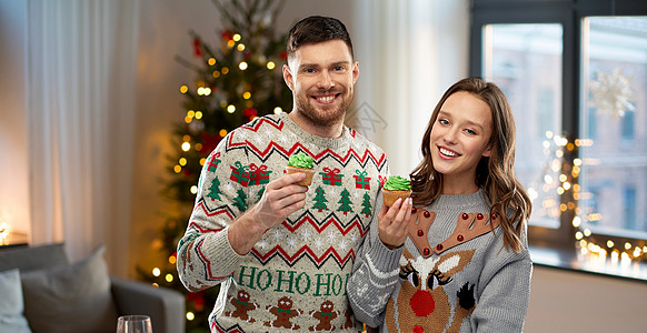 诞节,人假日的幸福的夫妇毛衣派与纸杯蛋糕家庭背景夫妇带着纸杯蛋糕穿着诞毛衣图片