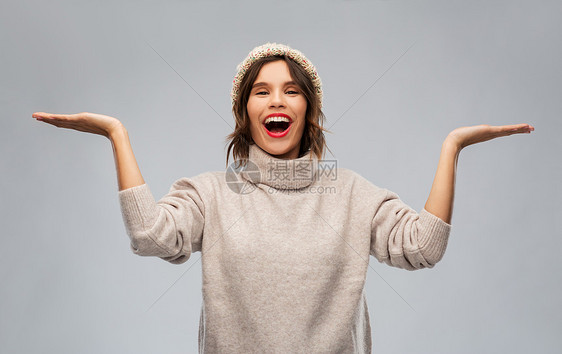 诞节,季节人们的快乐的微笑的轻女人,穿着针的冬帽毛衣,着些东西空空的手掌上灰色的背景戴着冬帽的轻女人图片