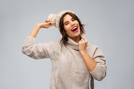 诞节,季节人们的快乐的微笑轻女子针冬帽毛衣灰色背景穿着针冬帽毛衣的轻女人图片