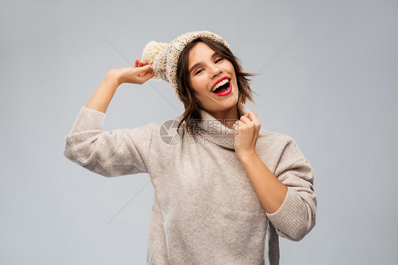 诞节,季节人们的快乐的微笑轻女子针冬帽毛衣灰色背景穿着针冬帽毛衣的轻女人图片
