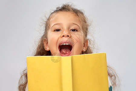 阅读,教育童的快乐的小女孩躲书后灰色的背景快乐的小女孩躲书后图片