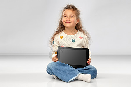 童人的美丽的微笑女孩与平板电脑坐地板上的灰色背景微笑的女孩,平板电脑坐地板上图片