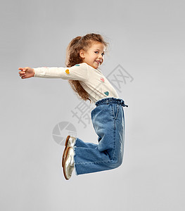 童,时尚人的微笑的小女孩穿着牛仔裤跳过灰色的背景微笑的小女孩跳跃图片